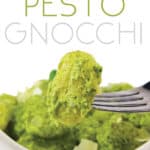 white bowl of creamy pesto gnocchi with a fork with gnocchi on it