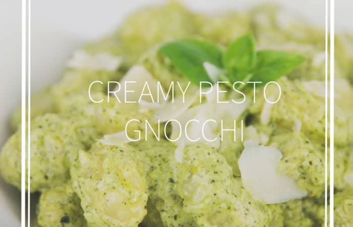 white bowl of creamy pesto gnocchi with shaved parmesan and basil leaf