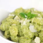 white bowl of creamy pesto gnocchi with shaved parmesan and basil leaf