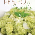 white bowl of creamy pesto gnocchi with shaved parmesan and basil leaf