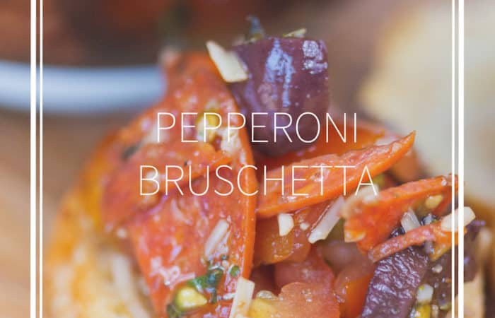 a crossonti with pepperoni, kalamata olives, parmesan cheese on wood cutting board with glass bowl of bruschetta