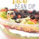 A clear bowl with layers of beans, guacamole, salsa, sour cream, lettuce, cheese, tomatoes, and olives