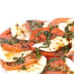 white plate of sliced tomatoes and mozzarella cheese with chopped basil and balsamic glaze on top