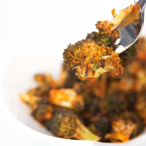 a white bowl of cooked broccoli with sriracha sauce on a fork