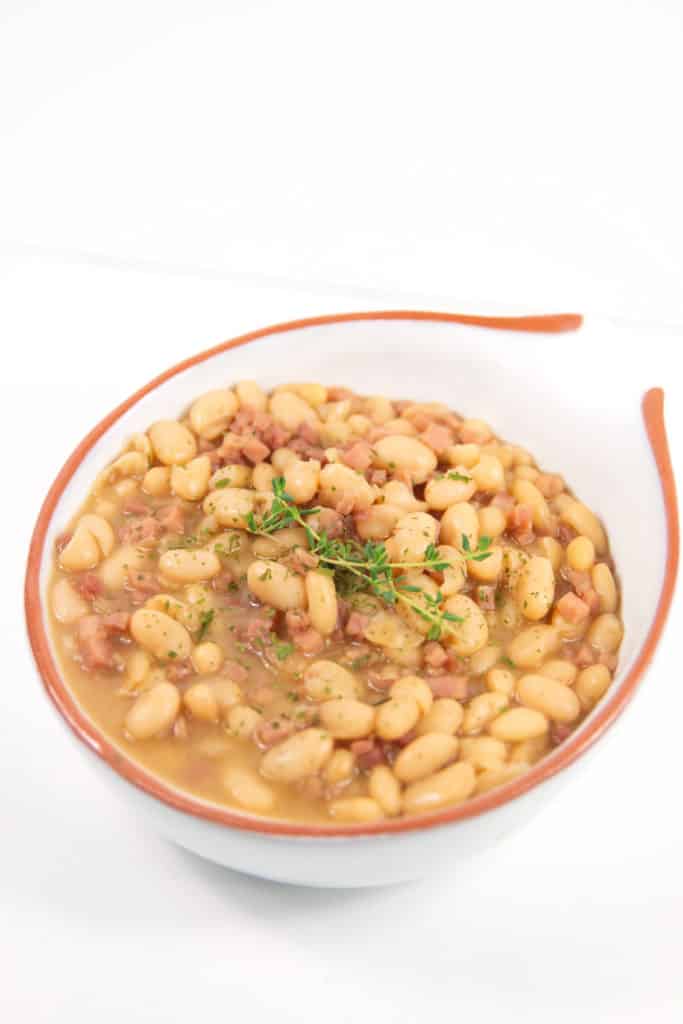 ham and bean soup in a white bowl with orange rim with thyme on top