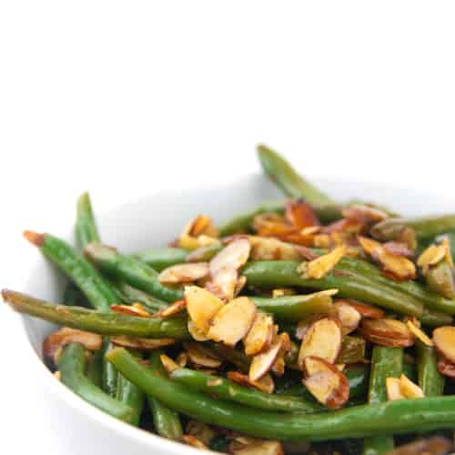 a white bowl of cooked balsamic green beans with almonds on top