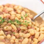 up close shot of ham and bean soup in a white bowl with thyme on top