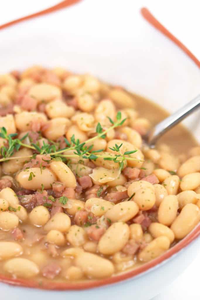 up close shot of ham and bean soup in a white bowl with thyme on top