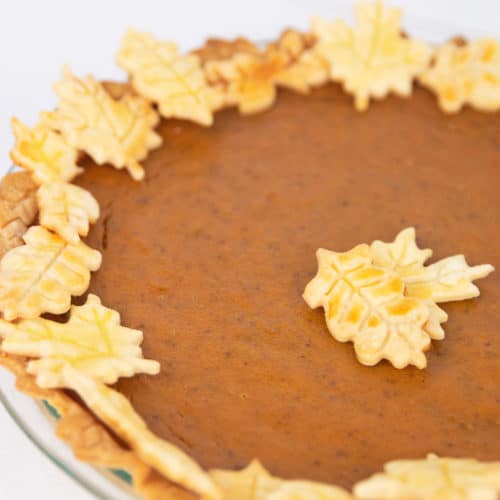 a pumpkin pie in a glass pan with leaf cut outs of crust