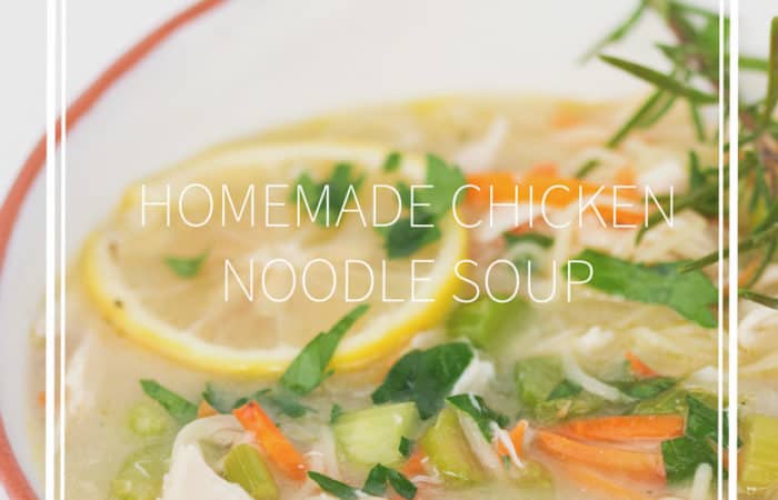 bowl of homemade chicken noodle soup with sliced lemons, parsley, and rosemary twig