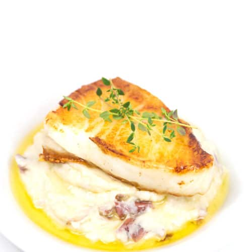 a plate of pan seared sea bass with mashed potatoes with a butter sauce and fresh herbs garnish
