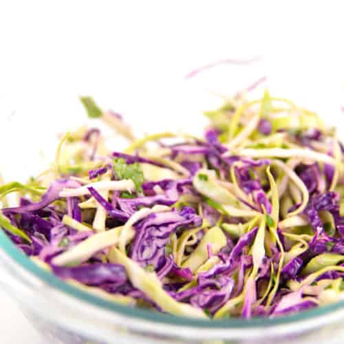 a glass bowl of green and red cabbage shredded for Mexican coleslaw