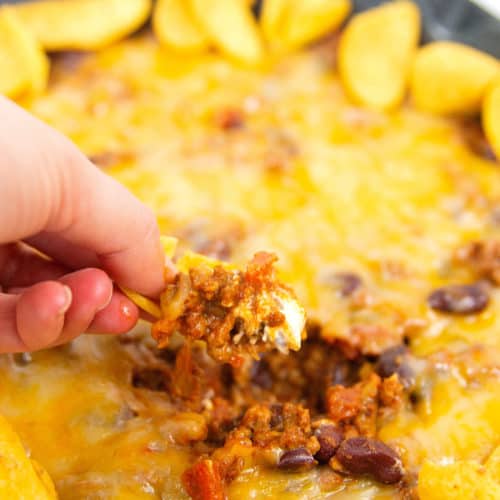 frito chili pie dip on a corn chip with dip in a pan in the background