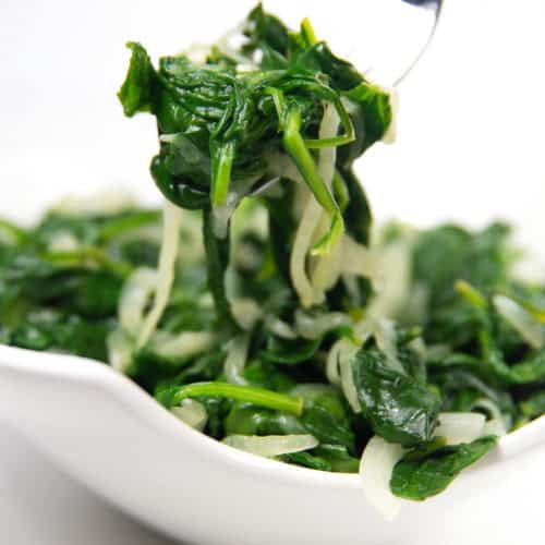 white bowl of sauteed spinach with caramelized onions with a fork with some on it