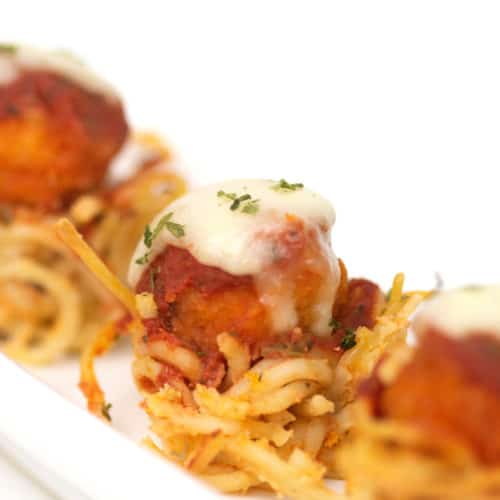 popcorn chicken with sauce and cheese on top of a bowl made of spaghetti on a white plate