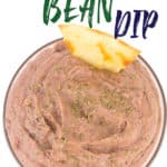 a glass bowl of black bean dip with parsley flakes on top with a tortilla chip sticking in it