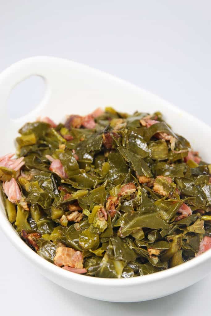 a white bowl of cooked collard greens with chunks of ham pieces