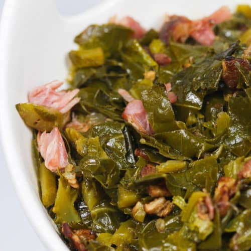 a white bowl of cooked collard greens with chunks of ham pieces