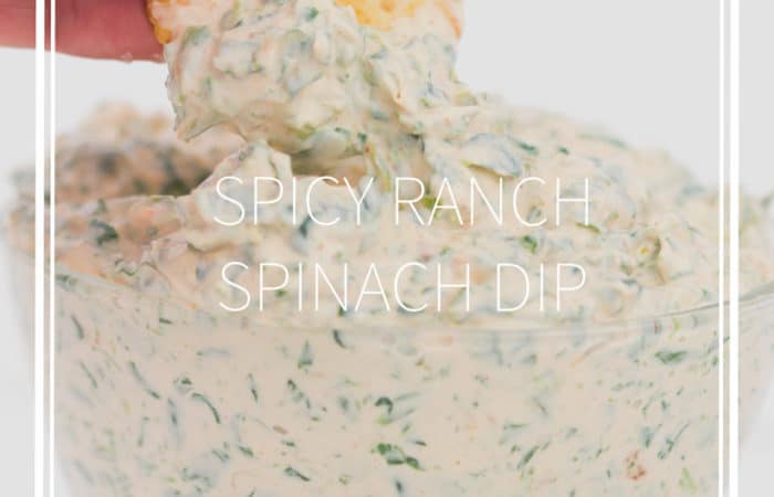 a glass bowl with spicy ranch spinach dip in it dipping a cracker in the dip
