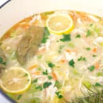 large pot of homemade chicken noodle soup with parsley, bay leaves, and sliced lemons