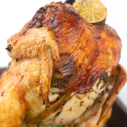 roasting pan with cooked whole chicken on a beer can with limes and cilantro