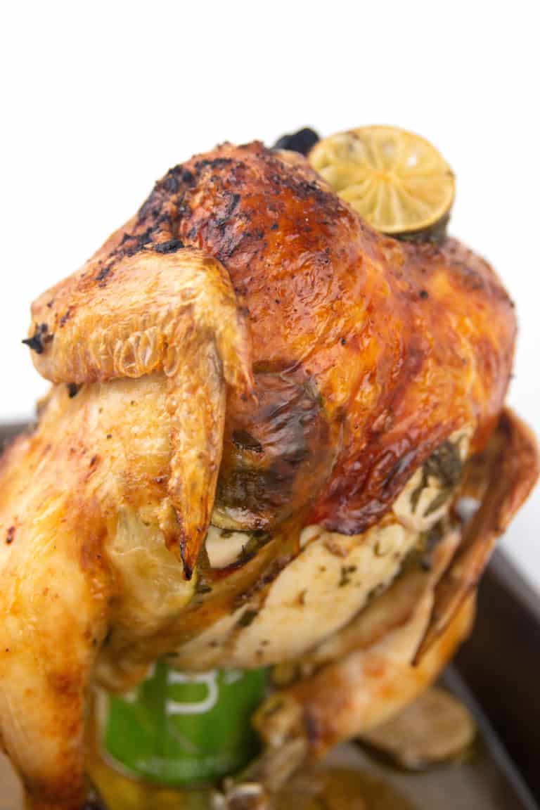 roasting pan with cooked whole chicken on a beer can with limes and cilantro
