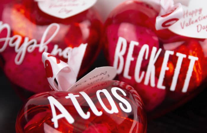 3 plastic red hearts filled with candy with names on them and ribbon on top