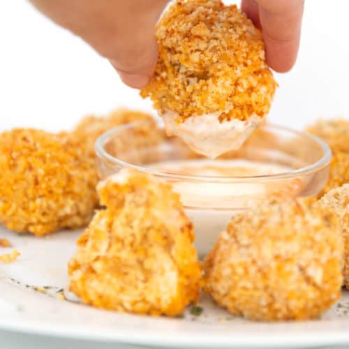 a white plate of buffalo chicken quinoa bites with a bowl of ranch dressing dipping in