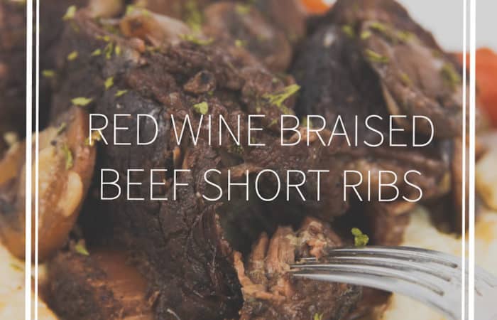 white plate of red wine braised beef short ribs over mashed potatoes with mushrooms, carrots, and sauce