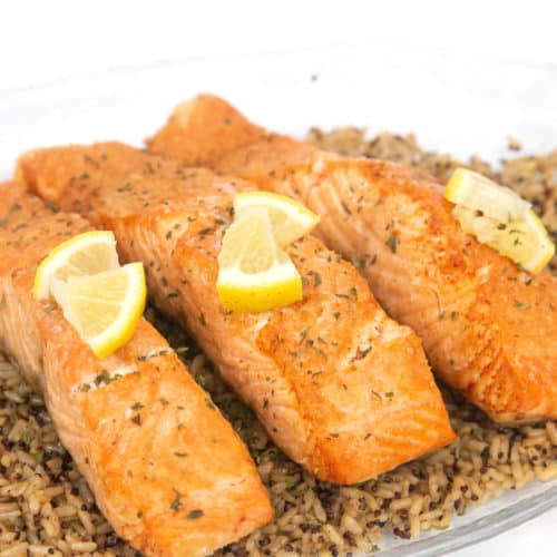 a glass plate of easy air fryer salmon pieces on top of brown rice with lemon on top of the salmon