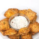 a white plate of air fried toasted spicy ranch ravioli with a bowl of ranch dressing dip