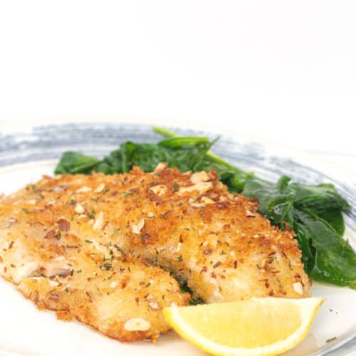 white and blue plate with almond crusted tilapia with a lemon slice and spinach