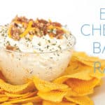 glass bowl of easy cheddar bacon ranch dip with cheese and bacon on top with chips around the bowl