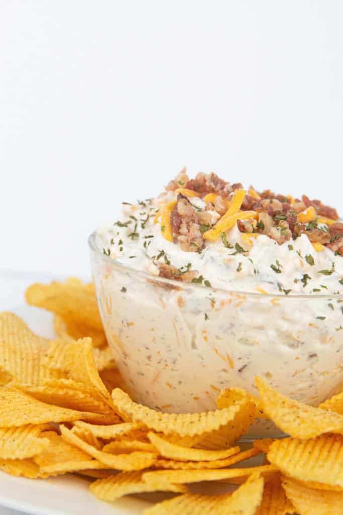 glass bowl of easy cheddar bacon ranch dip with cheese and bacon on top with chips around the bowl