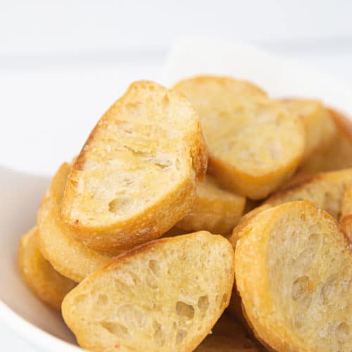 a white bowl of toasted baguette bread for easy crostini