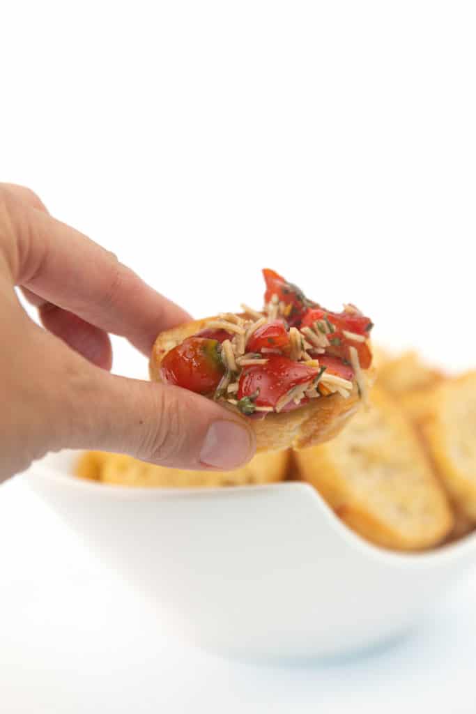 a piece of crostini with brushetta on top with a bowl of crostini in the background