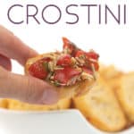 a piece of crostini with brushetta on top with a bowl of crostini in the background