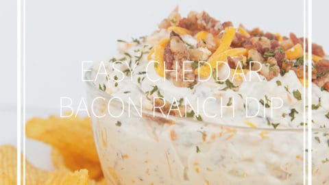 glass bowl of easy cheddar bacon ranch dip with cheese and bacon on top with chips around the bowl