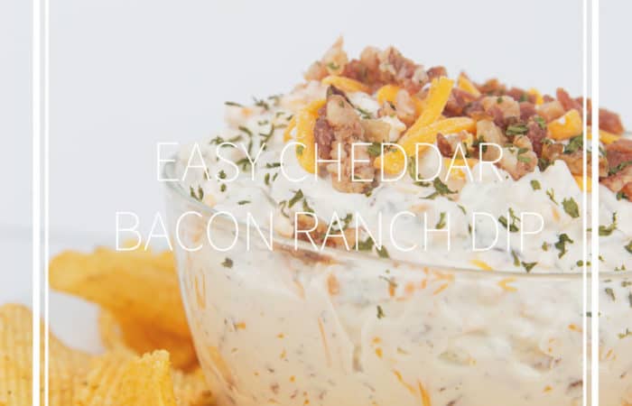 glass bowl of easy cheddar bacon ranch dip with cheese and bacon on top with chips around the bowl