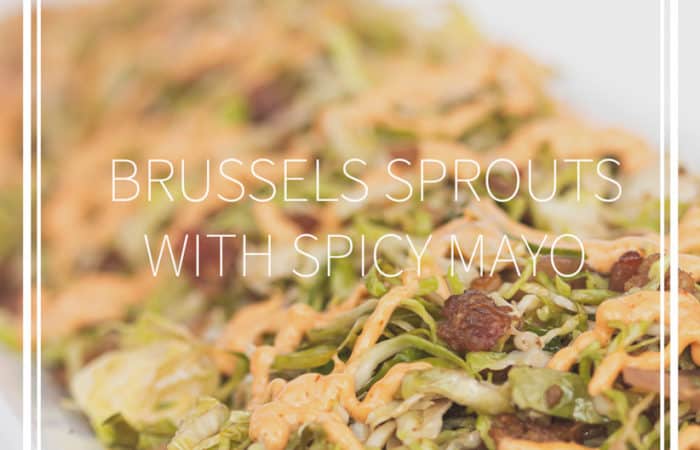 white plate of shaved brussels sprouts with spicy mayo drizzled on top