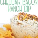 glass bowl of easy cheddar bacon ranch dip with cheese and bacon on top with chips around the bowl