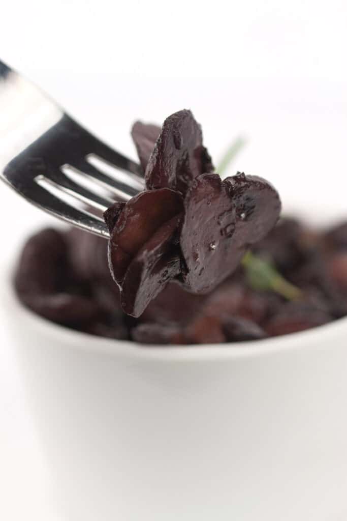 white bowl of sautéed truffle red wine mushrooms and a fork with the mushrooms on it