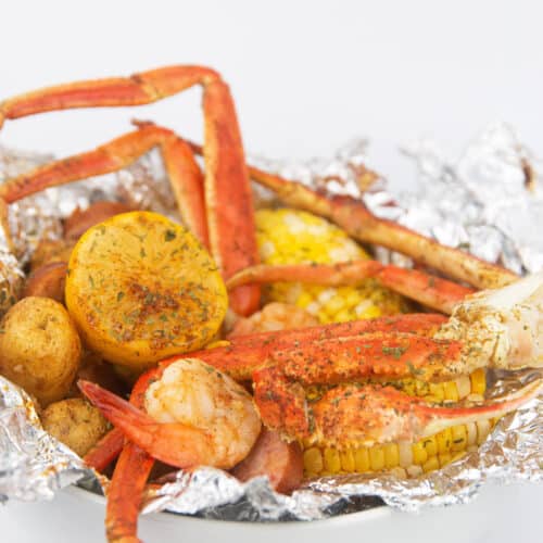a white bowl of seafood, corn, potatoes, sausage and lemon in foil for seafood cajun boil packs