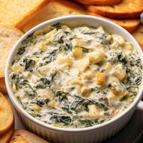 a bowl of Gourmet Fresh Spinach and Artichoke Dip with toasted bread around it