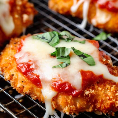 crispy baked chicken parmesan with melted cheese on a baking rack with basil garnish