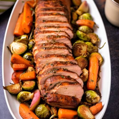 large serving dish of Herb Roasted Pork Loin with apples, carrots and brussels sprouts