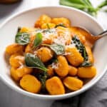 a white bowl of Decadent Pumpkin Gnocchi with sage and parmesan cheese garnish on top