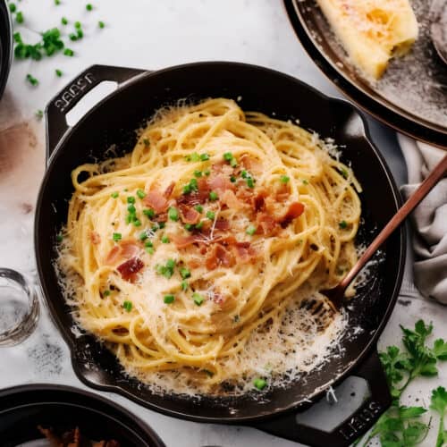 a cast iron pan of Budget Carbonara Bliss with green garnish on top with a wooden spoon